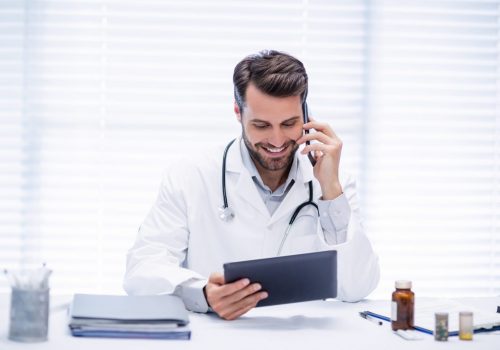 Male doctor talking on mobile phone while using digital tablet in clinic